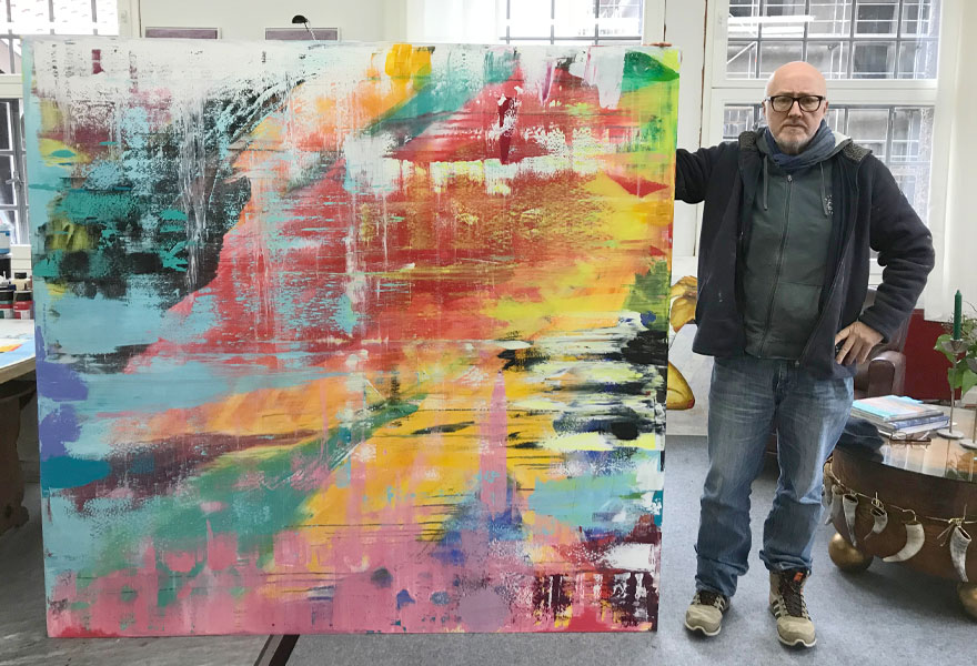 Der Künstler Holger Mühlbauer-Gardemin steht in seinem Atelier neben seinem gemalten fast 2x2 Meter großem Bild mit dem Namen "Abstrakt".